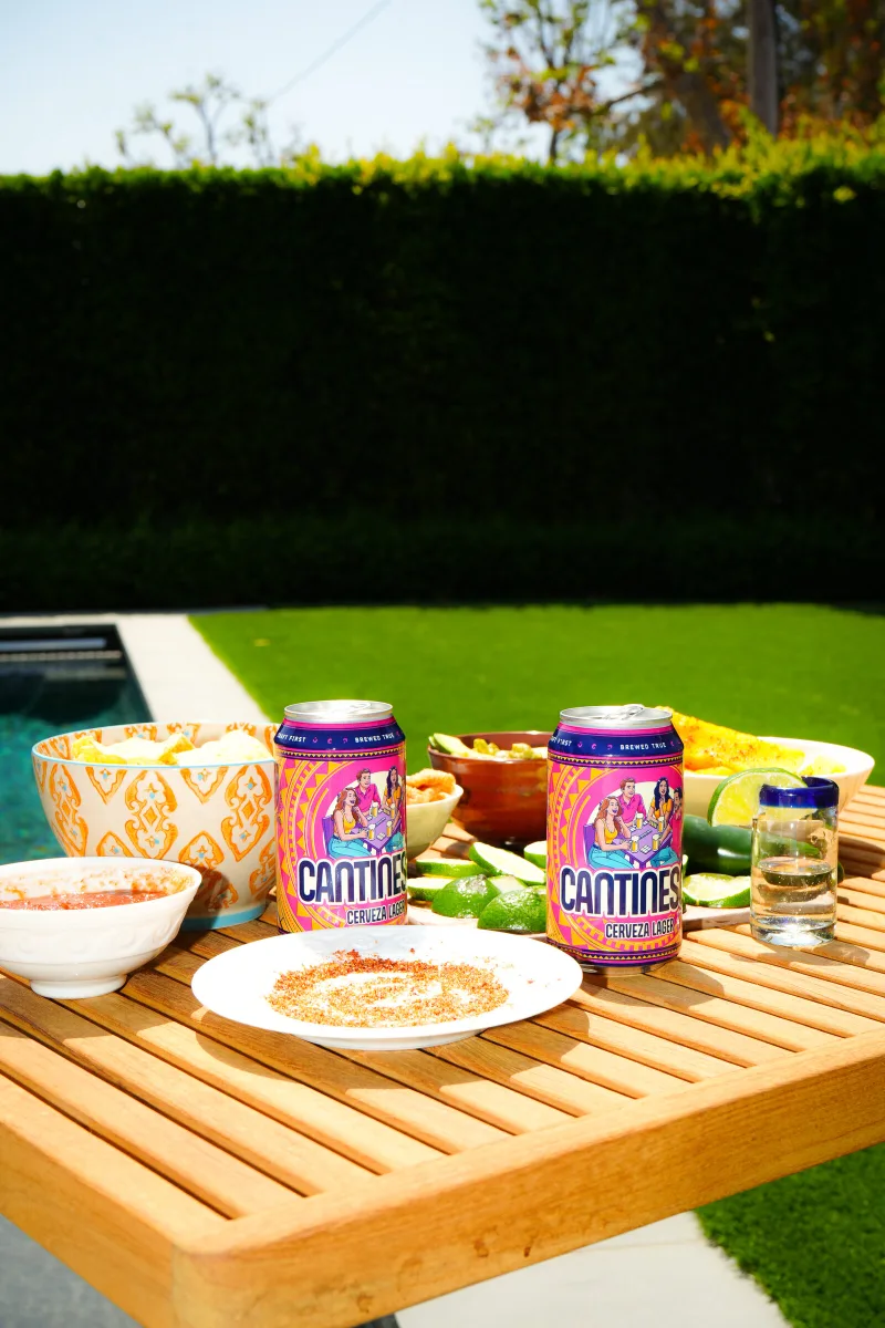 Two Cantinesca cans on a poolside table with chips and salsa